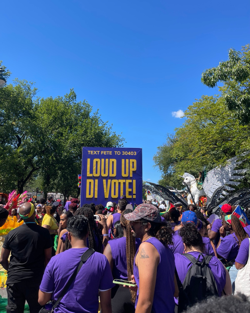 Folks holding sign that reads: 'Louding up di' vote at the Caribbean Parade
